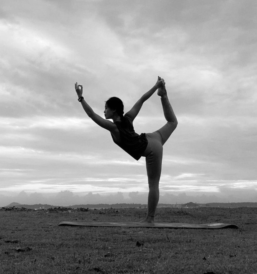 Mae, founder of Ommaega, holding dancer pose at dawn on open ground